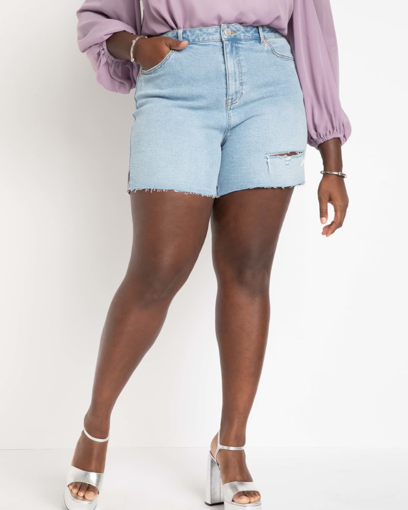 Side of a model wearing a size 22 Distressed Split Hem Shorts in Light Wash by ELOQUII. | dia_product_style_image_id:284376